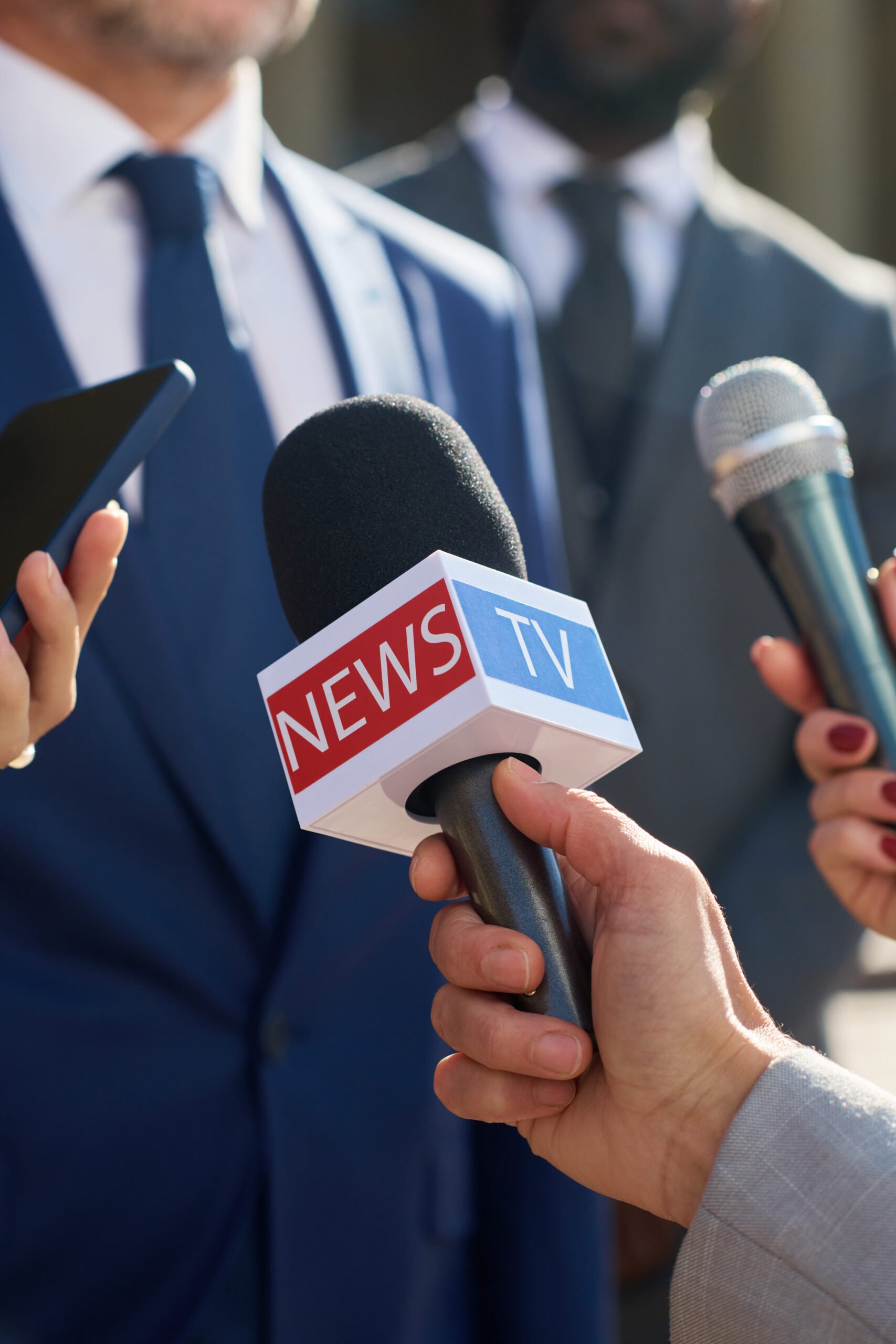 Interview setup with multiple microphones, including a TV news mic, at a corporate press conference.