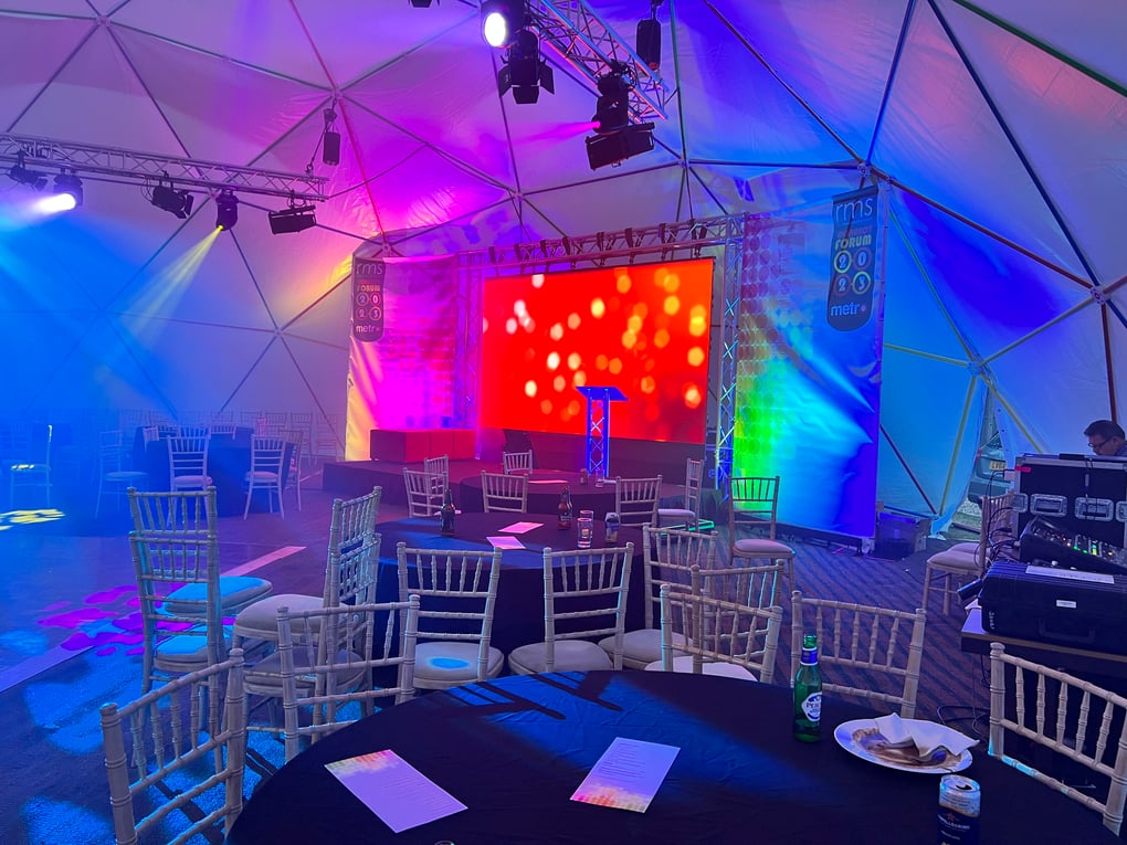 Geodesic dome setup for a corporate event with colorful stage lighting, large LED screen, and arranged seating.