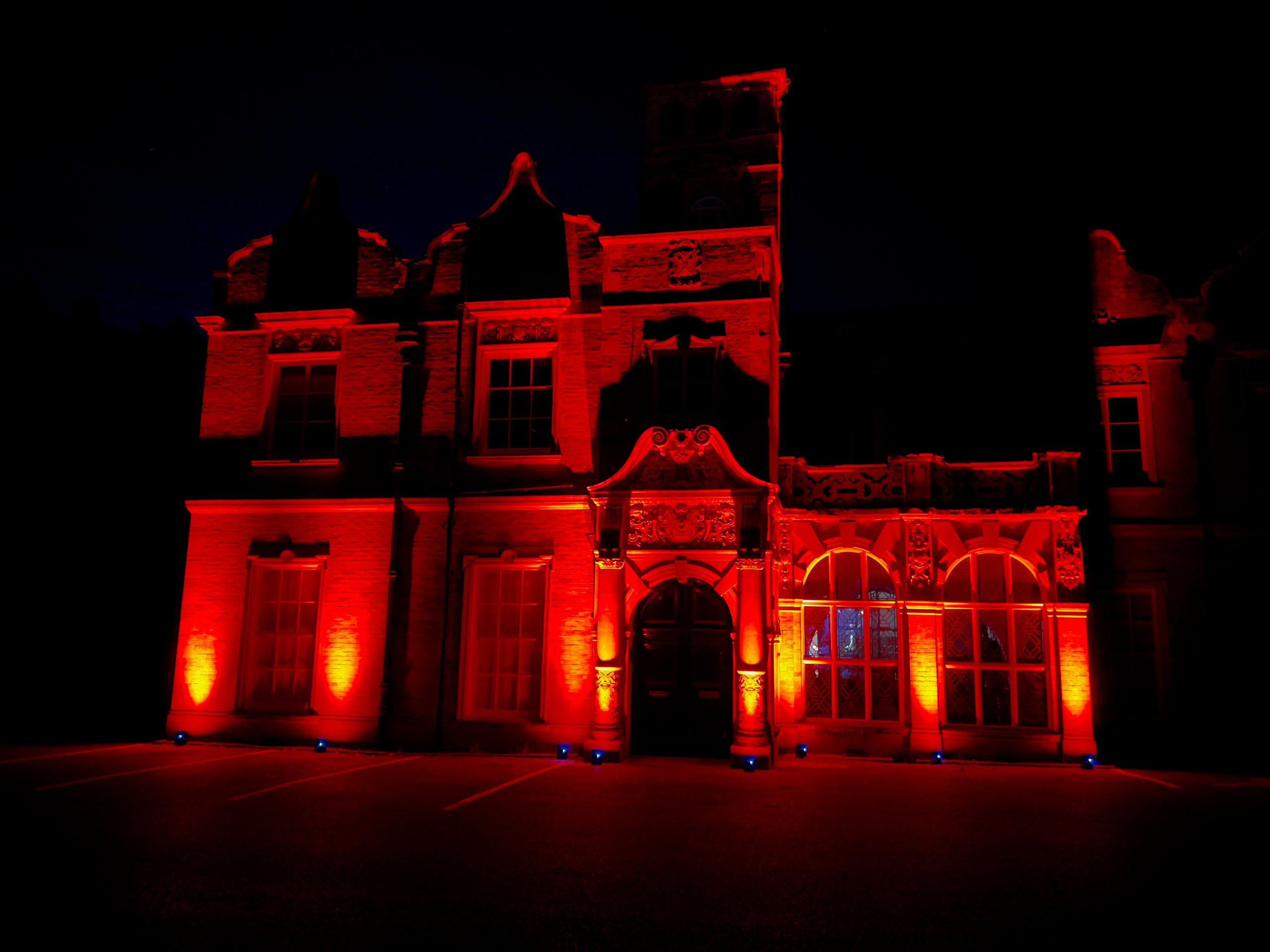 Historic building facade illuminated with dramatic red uplighting, creating a striking atmosphere for an evening event.