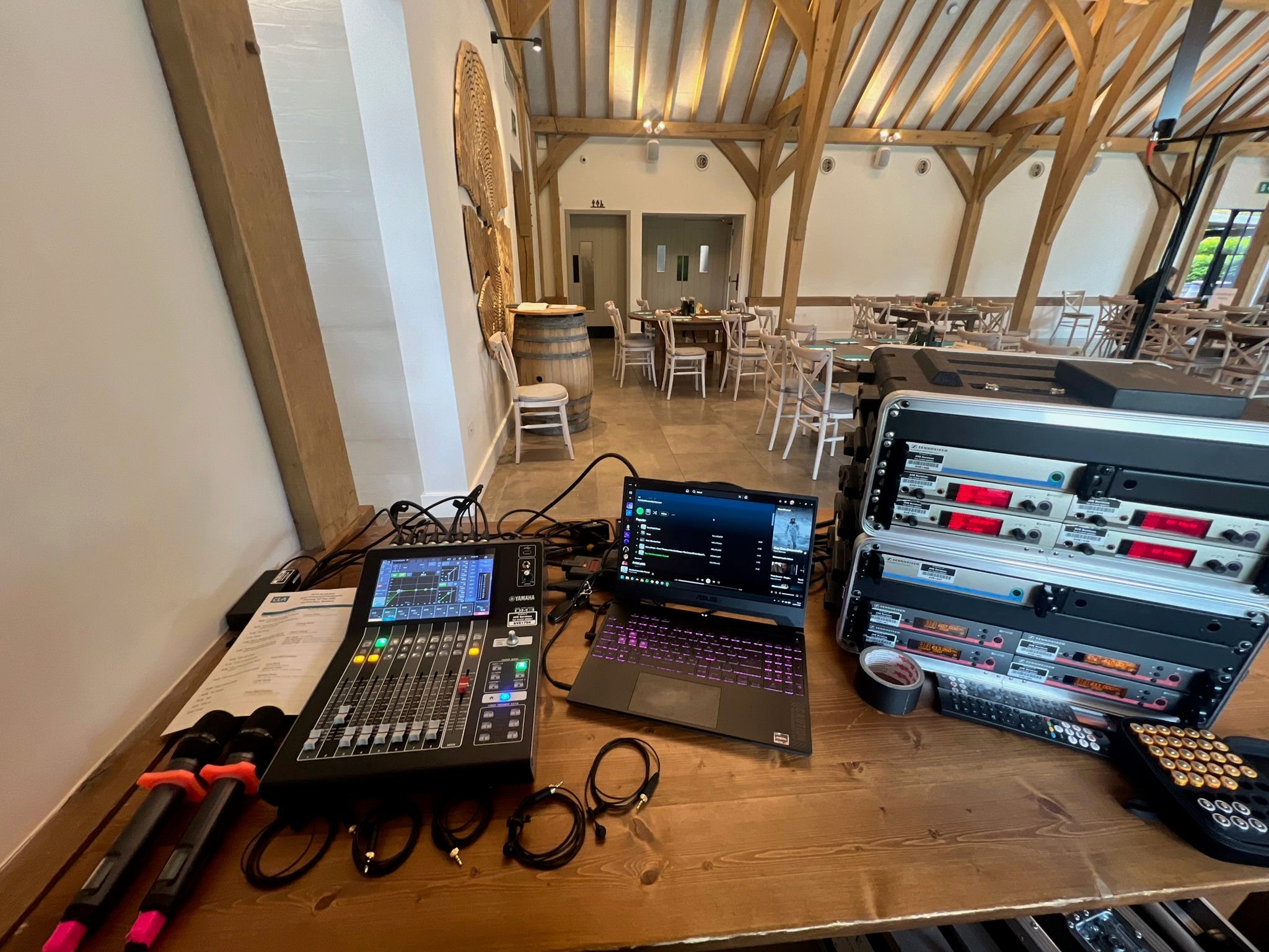 Sound and lighting control setup for a corporate event in a wooden-beamed venue, featuring mixing console and wireless microphones.
