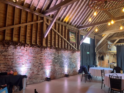 Rustic event space with uplighting on brick walls, set up for a corporate conference with round tables and chairs.