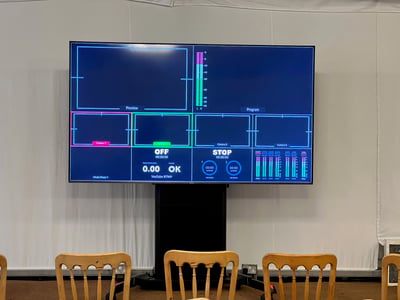 Large screen displaying AV control interface setup for a corporate conference, with wooden chairs arranged in front.