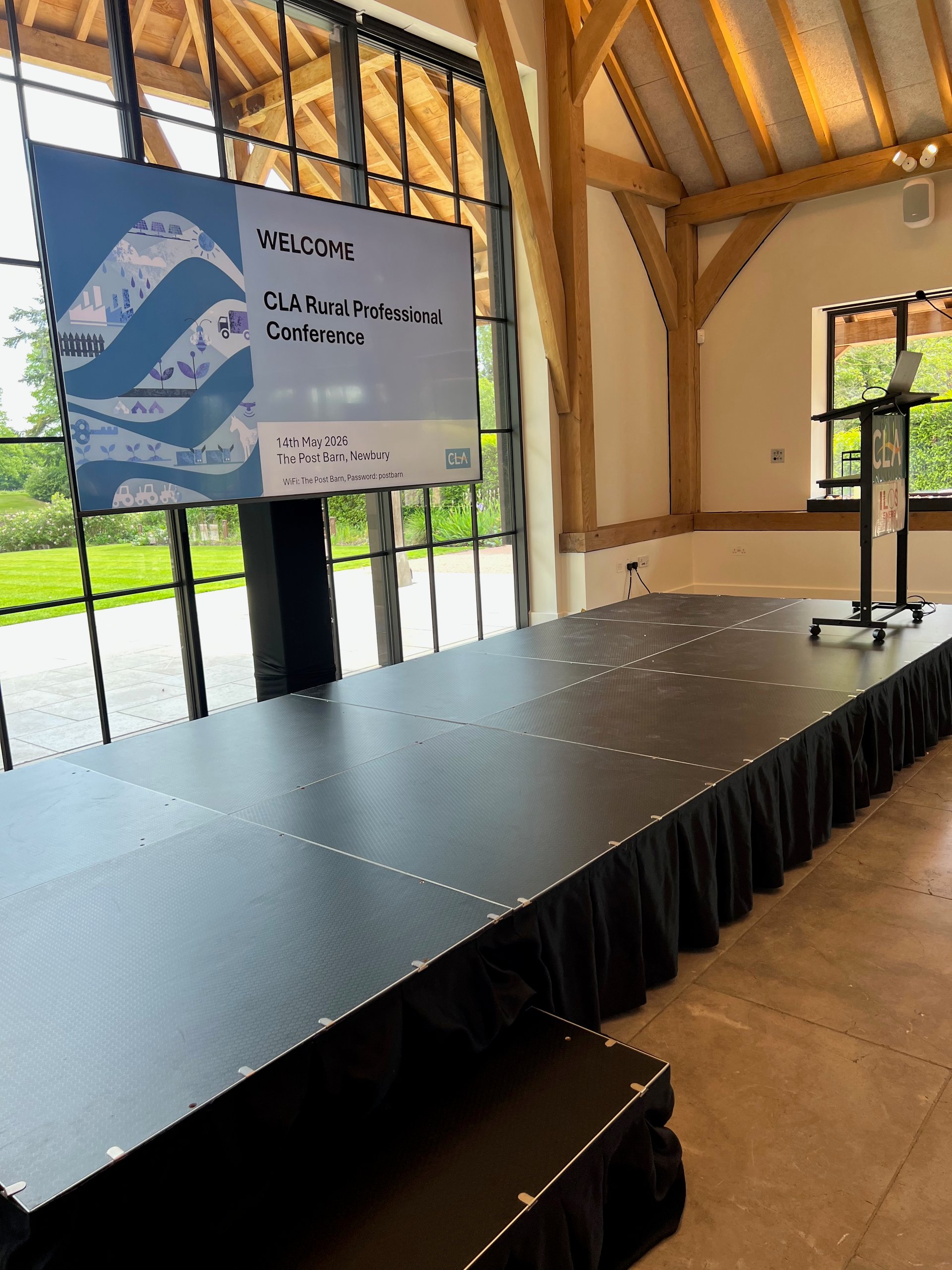 Staging setup for CLA Rural Professional Conference at The Post Barn, Newbury, featuring a projector display and a lectern.