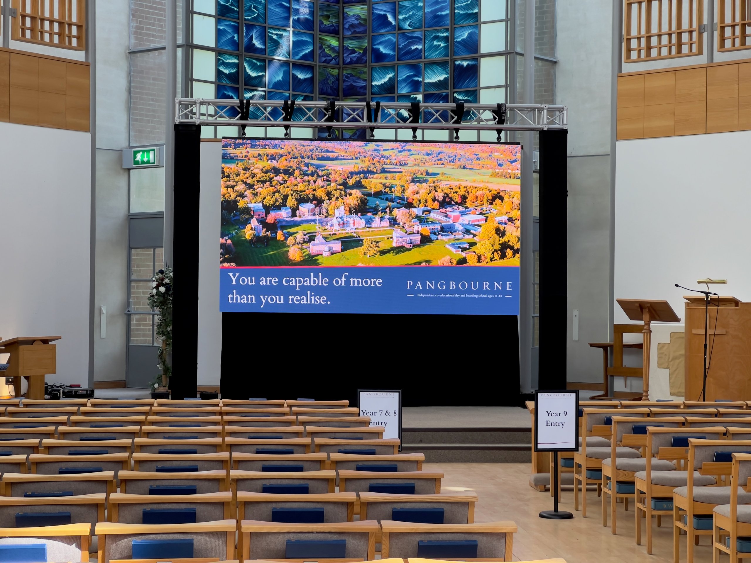 Church hall setup with tiered seating and large screen displaying Pangbourne campus image, ideal for corporate conferences.