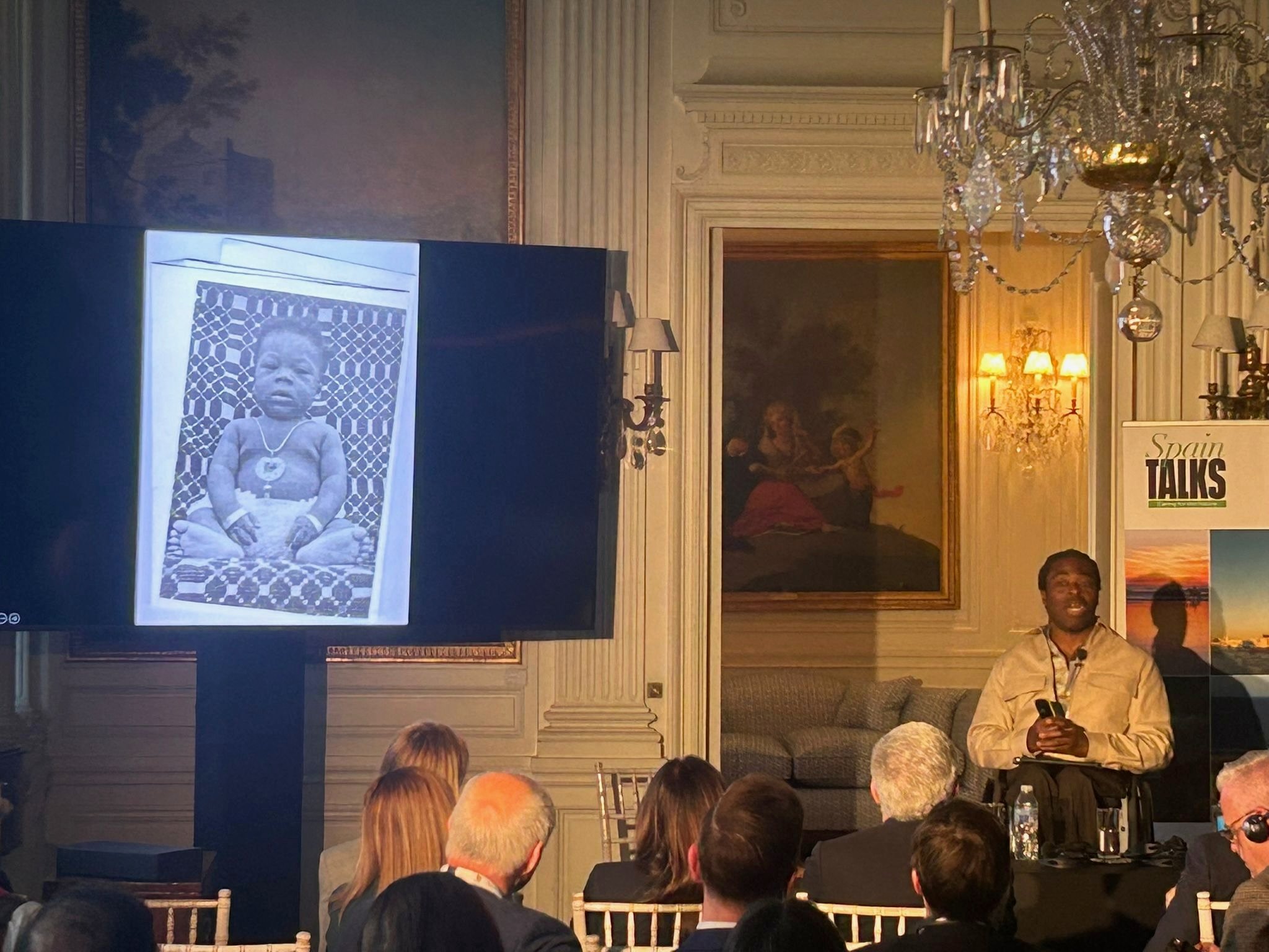 Speaker at a Spain Talks conference in an elegant hall, presenting with audiovisual support and large screen display.