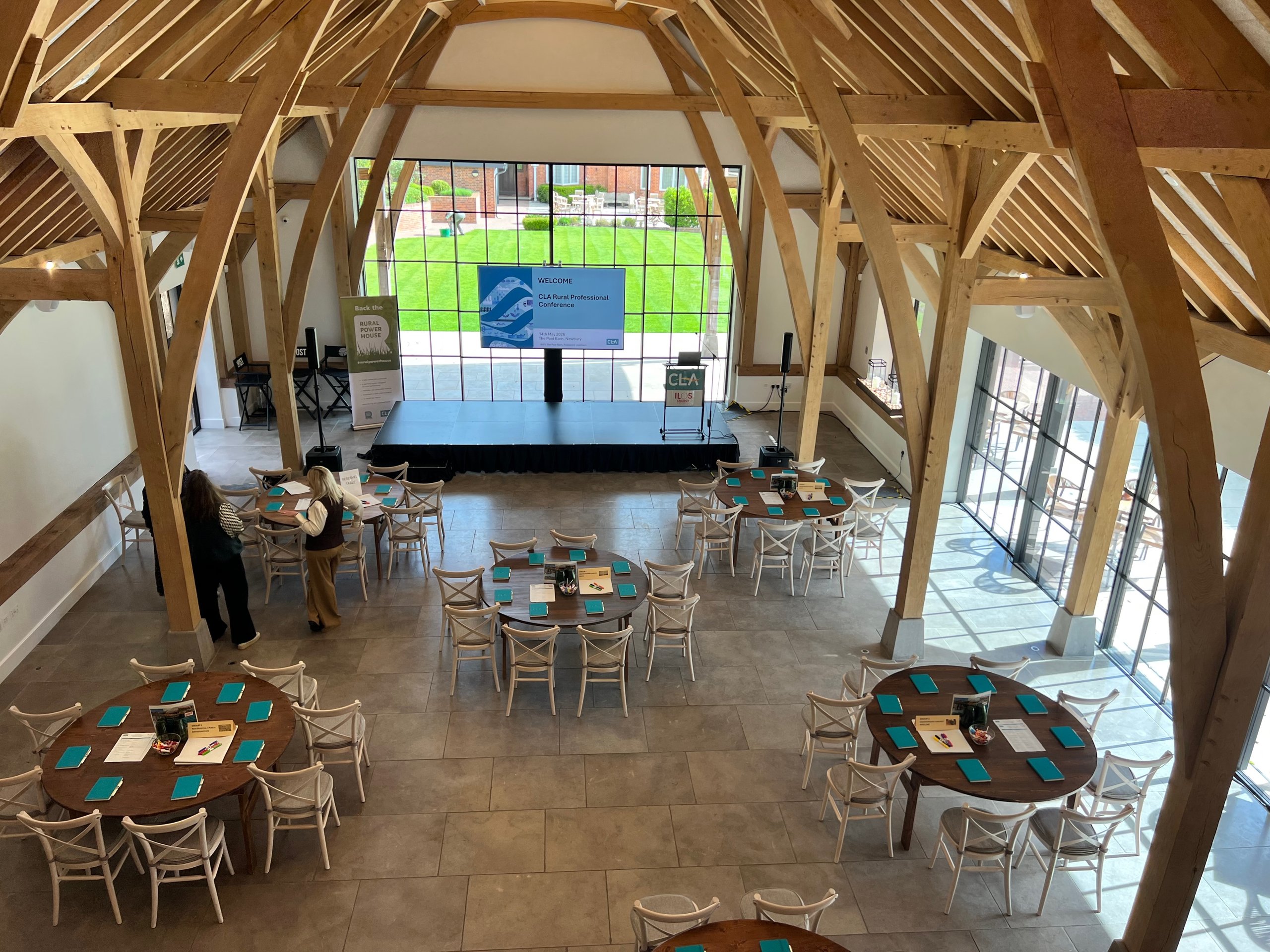 Rustic barn venue setup for a professional conference with round tables, a presentation stage, and AV equipment.