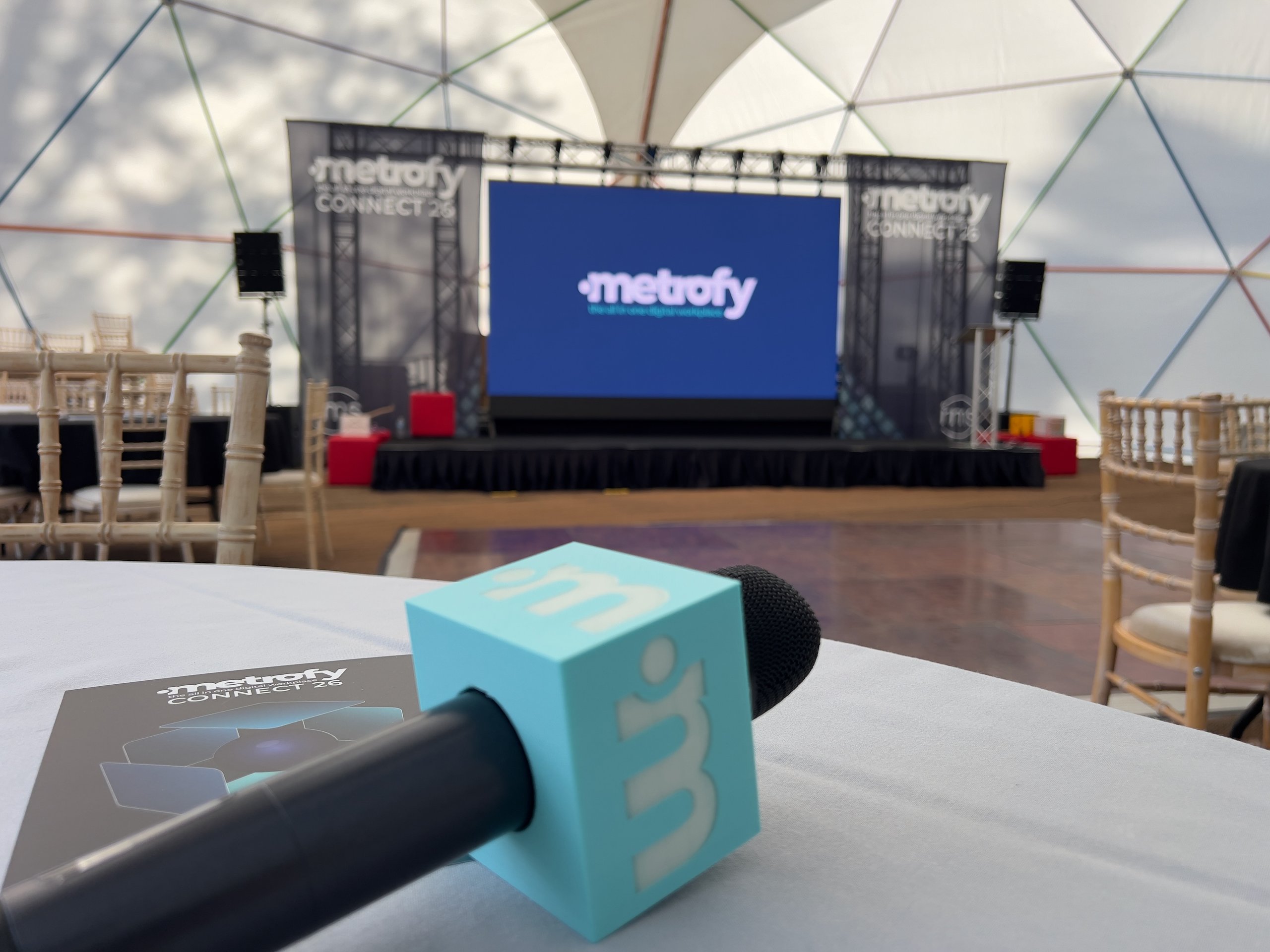 Microphone setup in front of stage at a corporate conference, featuring large screen and seating in a dome venue.