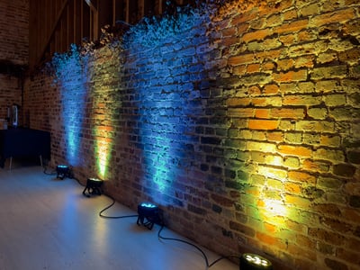 Uplighting illuminates a rustic brick wall with colorful beams, ideal for weddings or corporate events.