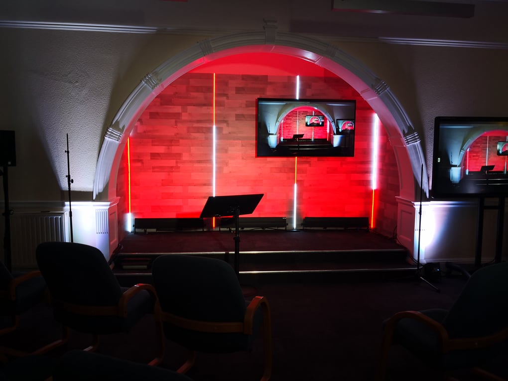 Staging setup with red LED lighting and displays in an archway for a corporate conference presentation.