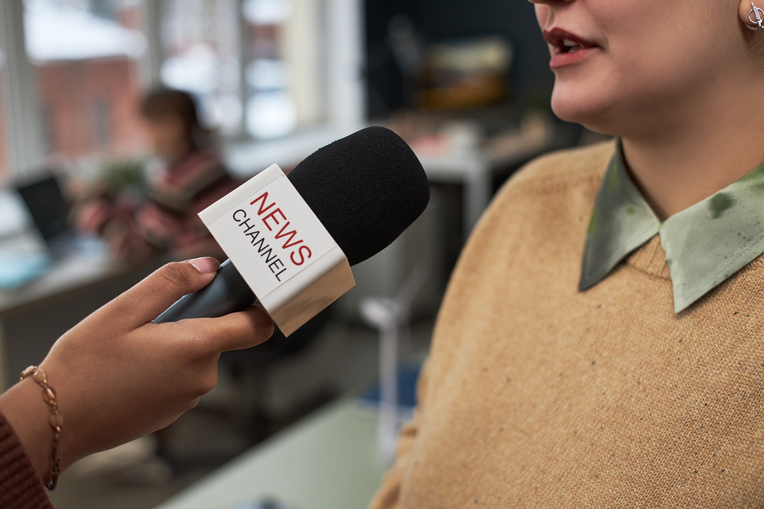 Interview setup with a microphone labeled News Channel held near a speaker, suggesting a corporate event or press conference.