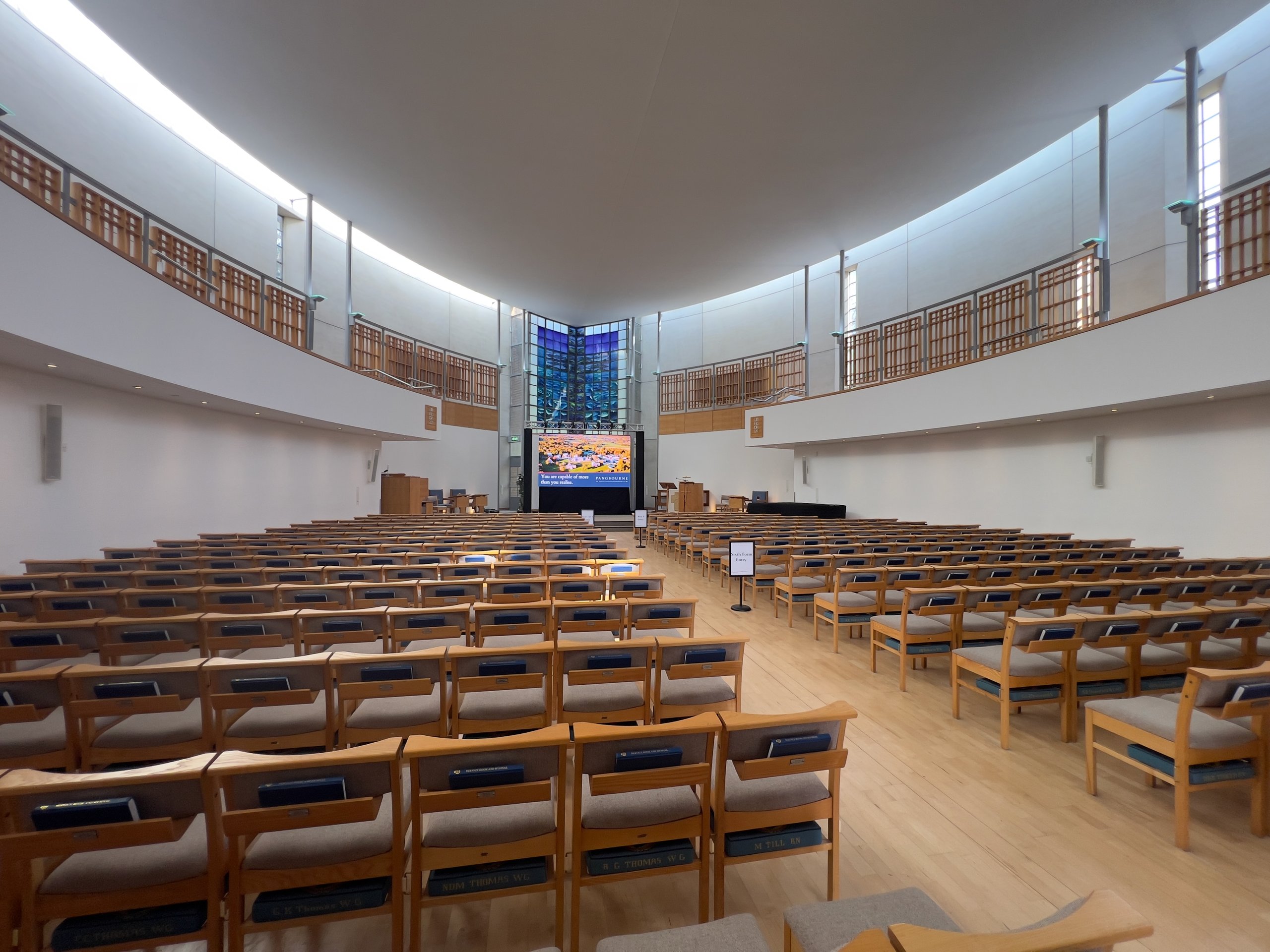 Rows of seating arranged for a corporate conference in a modern auditorium featuring a digital display and podium at the front.