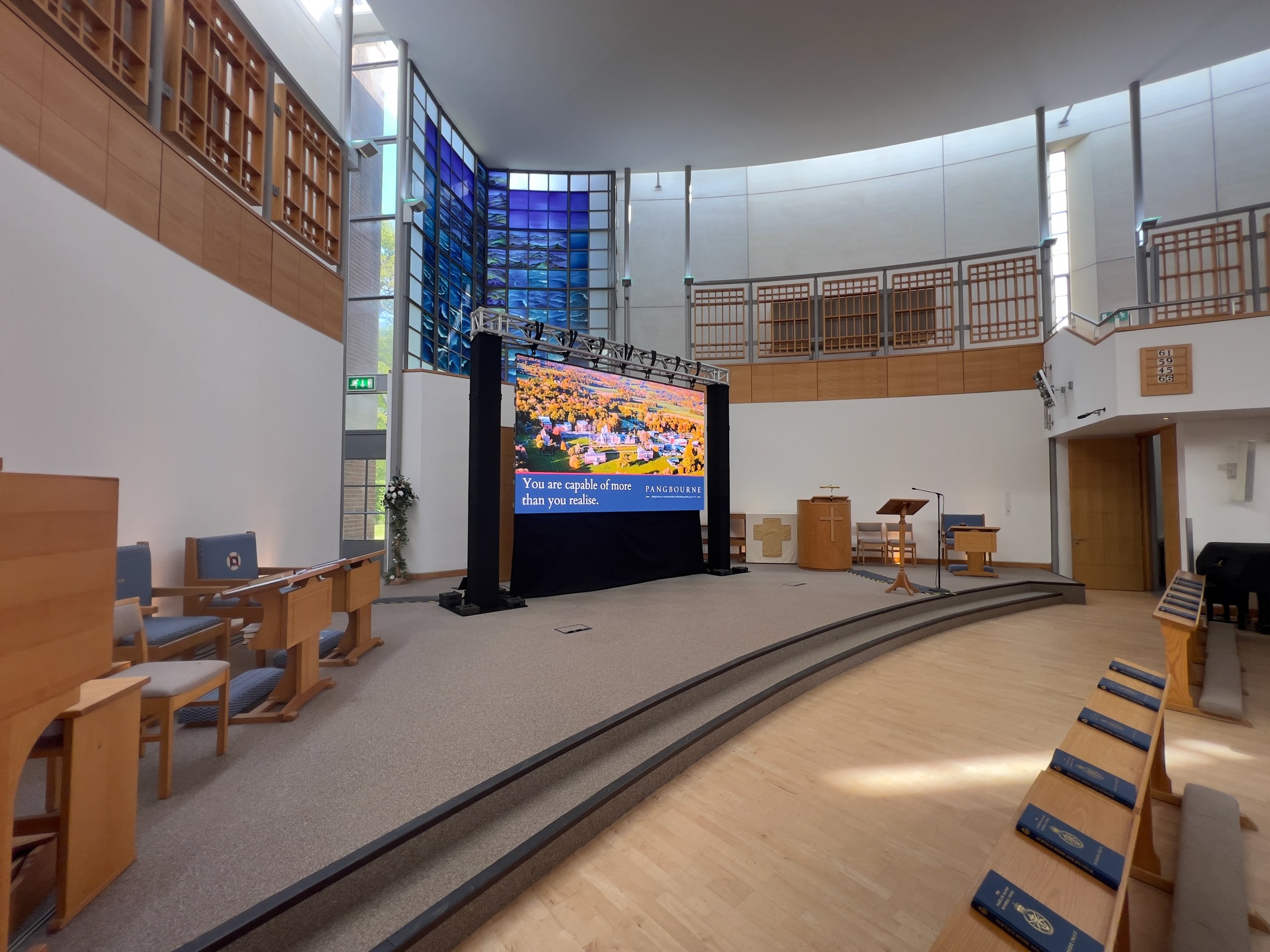 Church interior with AV setup including a large LED screen displaying colorful visuals, lectern, and seating for a conference.