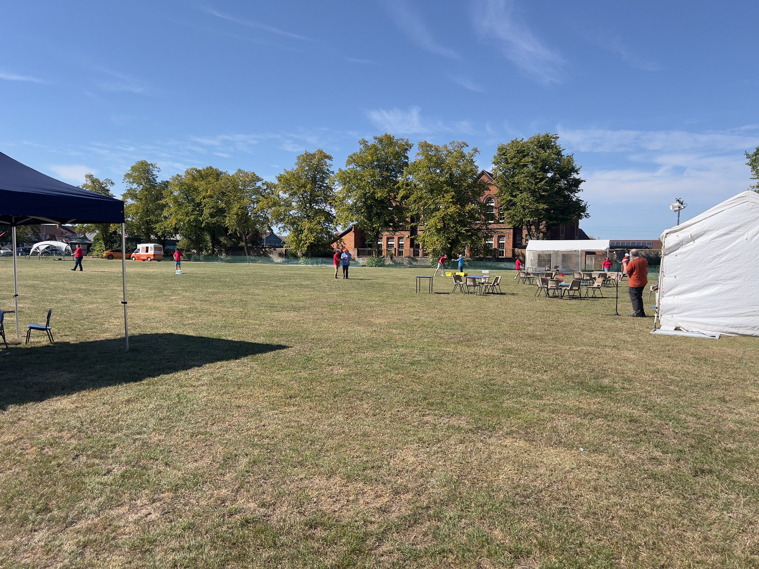 Outdoor team-building event setup with canopy tents, folding tables, and chairs on a grassy field near a historic building.