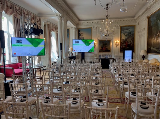 Conference setup in an elegant room featuring rows of chairs, stage lighting, and AV screens displaying Spain Talks.