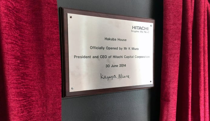 Plaque unveiling ceremony with red velvet curtains for Hakuba House, opened by Hitachi CEO. Event production setup visible.