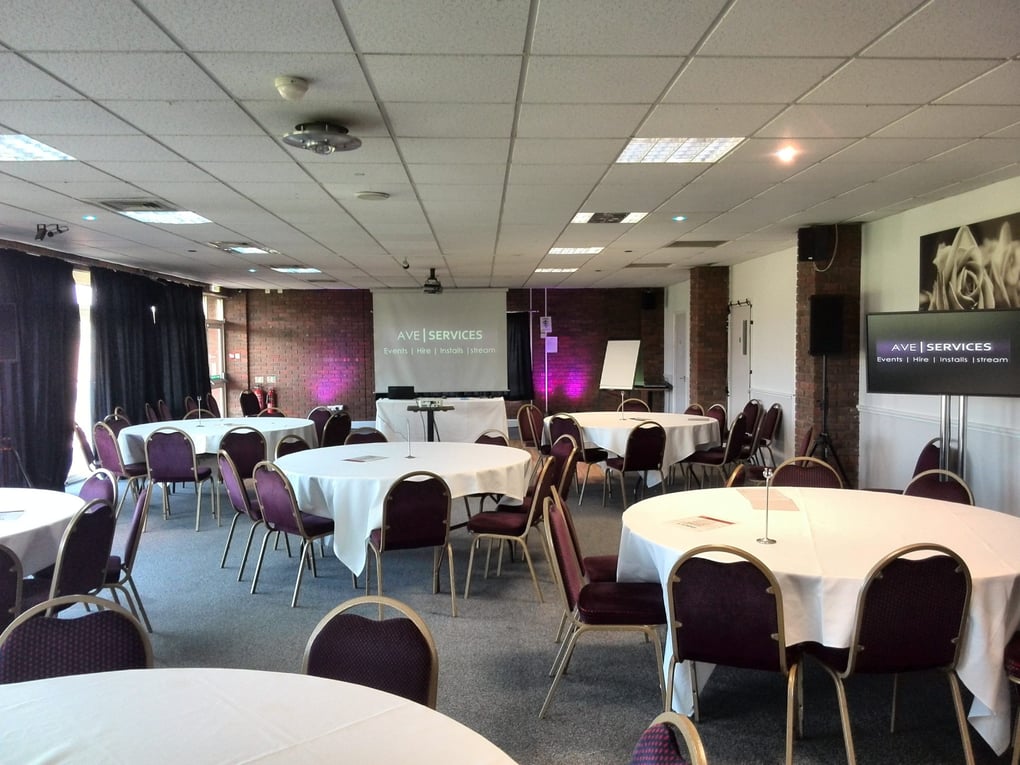 Conference room setup with round tables, projection screen, and AV equipment by AVE Services. Suitable for corporate events.