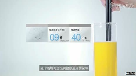 A hand stirs a glass of orange juice with black straws, displaying nutritional details in Chinese characters nearby.