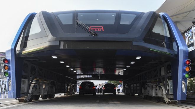 Futuristic public transport tram runs above cars on a busy road, showcasing innovative urban transit solutions.