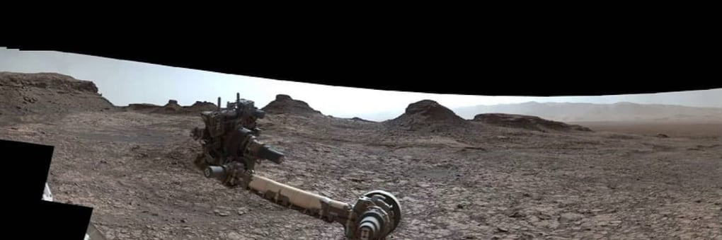 Mars rover exploring a barren, rocky landscape with distant mountainous formations, under a clear sky.