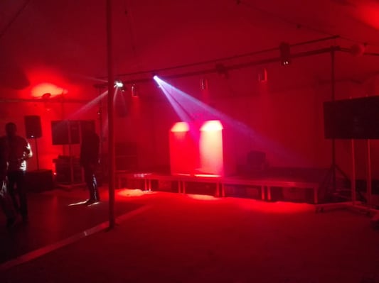 Red uplighting casts a vibrant glow on a stage setup for an evening event, highlighting the sound and lighting equipment.