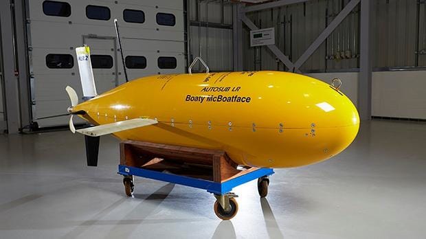 Yellow research submarine displayed in an indoor facility, resting on a transport trolley with industrial doors in the background.