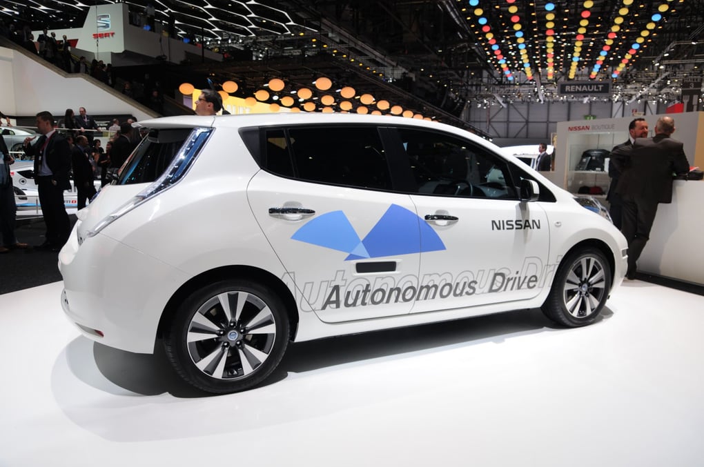 A white autonomous display car featured at an automotive exhibition, with ambient lighting and attendees discussing nearby.