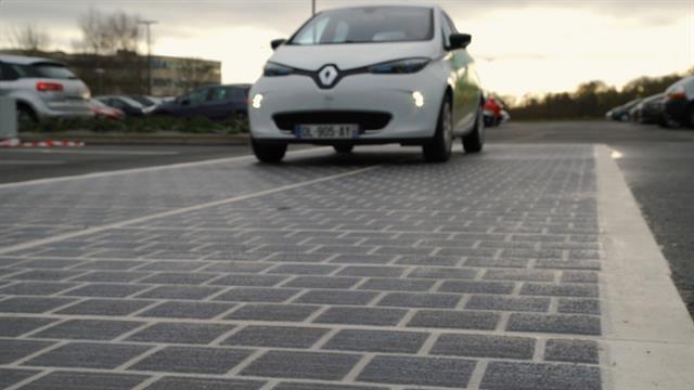 Electric vehicle driving on solar panel road in a parking lot, highlighting sustainable technology used in event production.