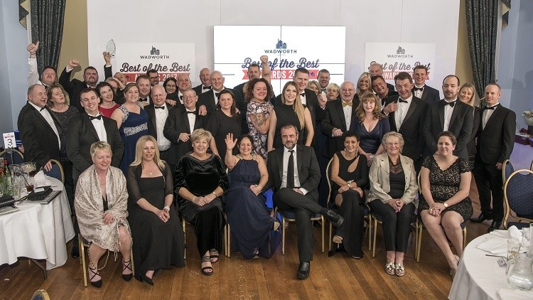 Formal group celebrating at an awards night with staging and event lighting. Participants in evening wear gathered around, smiling.