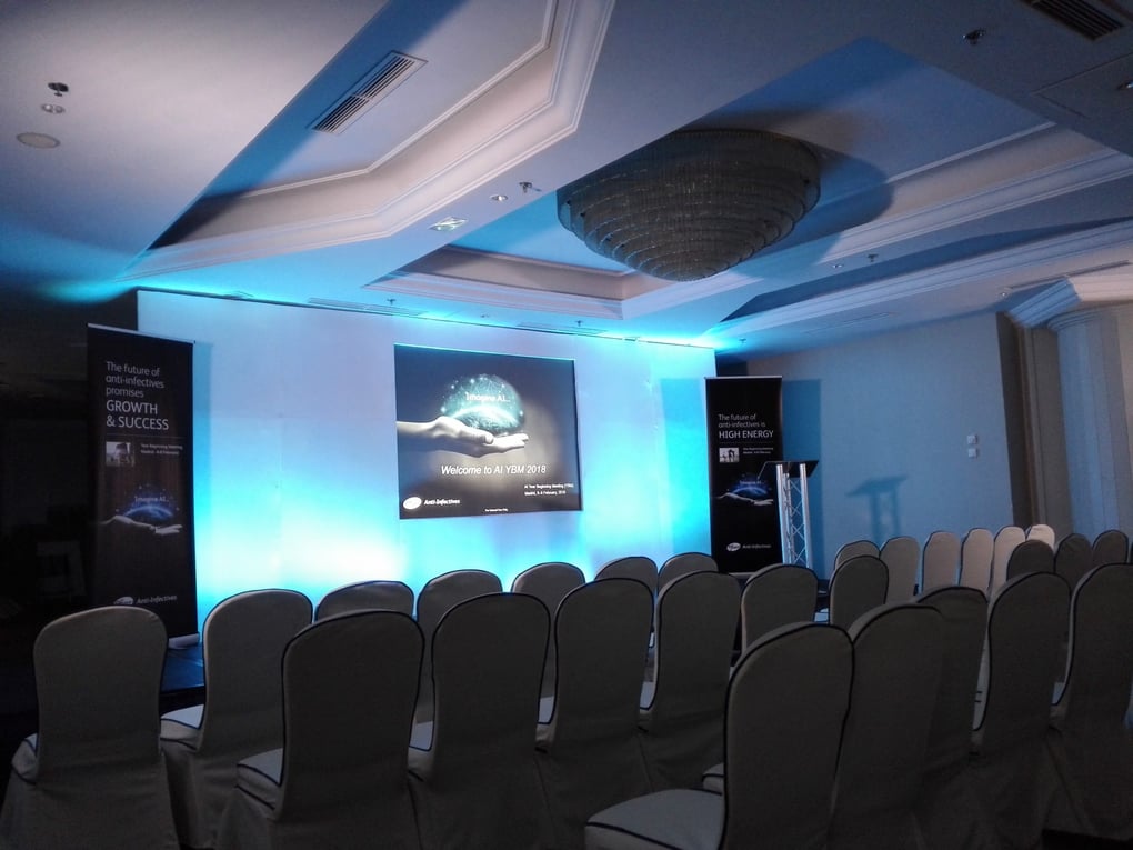 Conference setup with projector screen and banners, highlighting AV services in a corporate setting, with rows of chairs arranged.