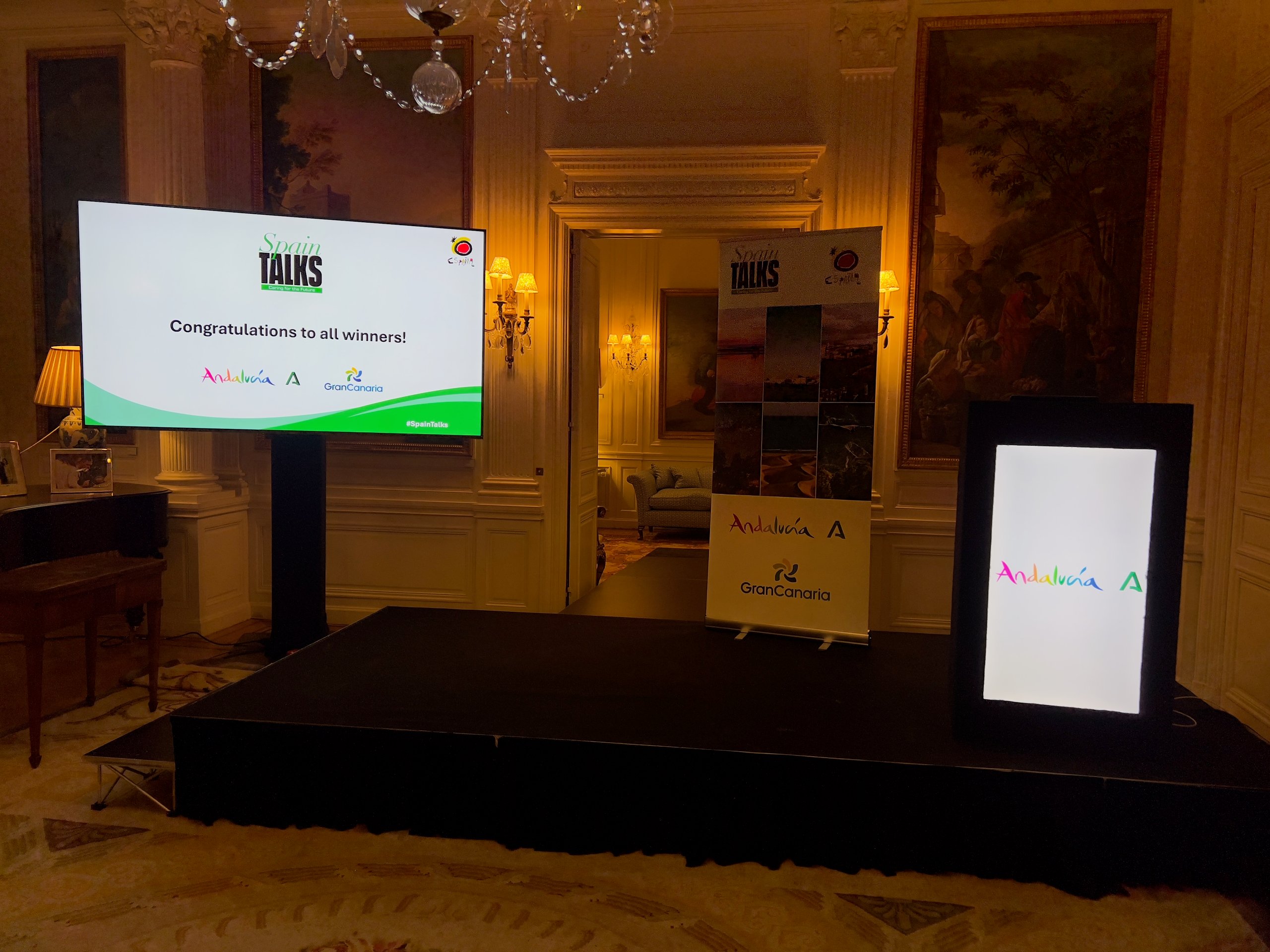 Staging setup for a corporate event with two large display screens and a banner showcasing Andalucía and Gran Canaria logos.
