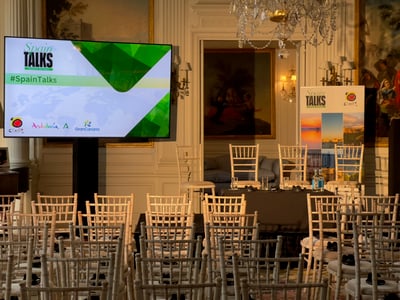 Conference room setup with a large display screen showing Spain Talks and event branding, ready for a panel discussion.