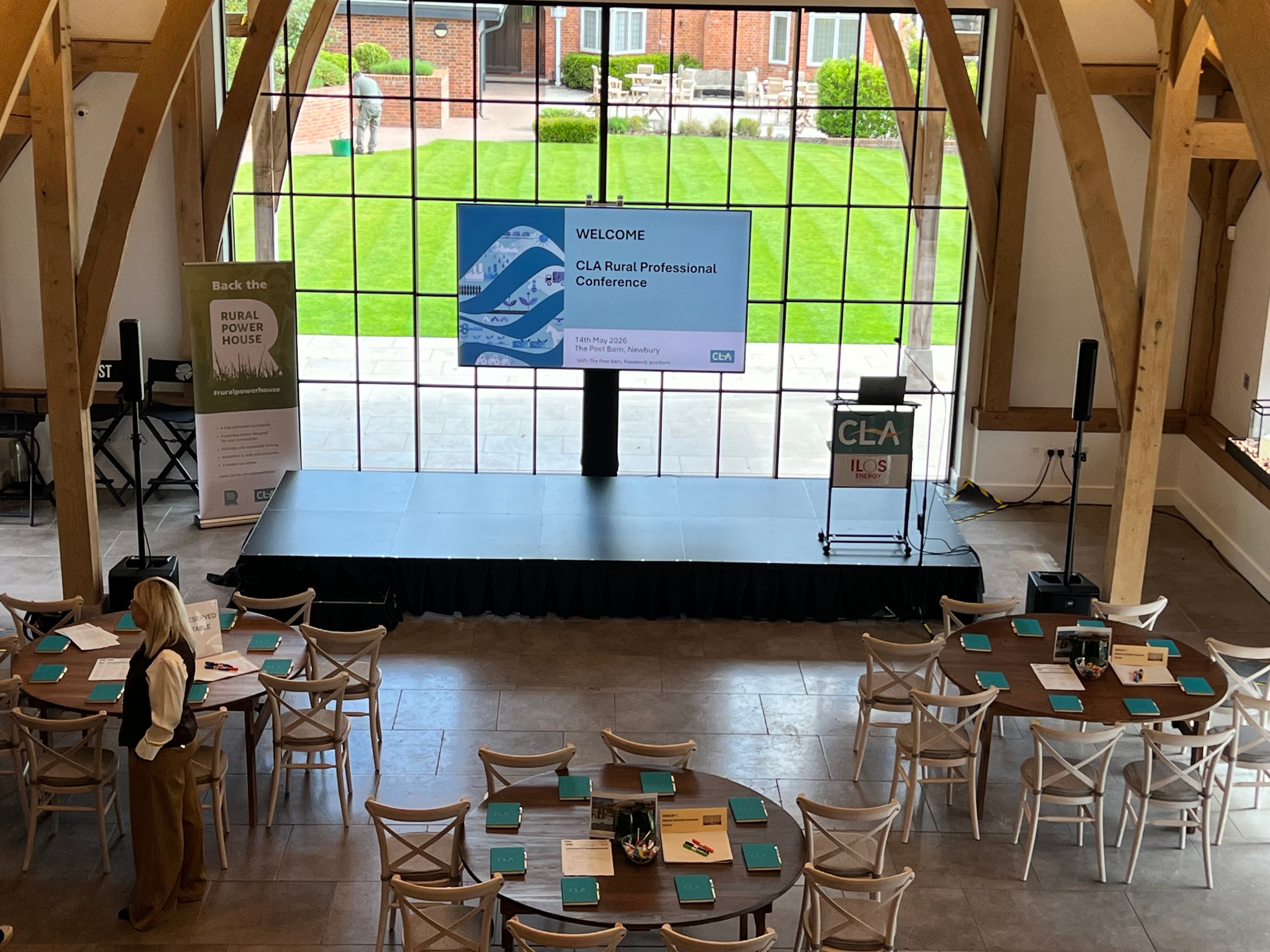 Staging setup for rural conference with podium, projector screen, and round tables in a barn venue.