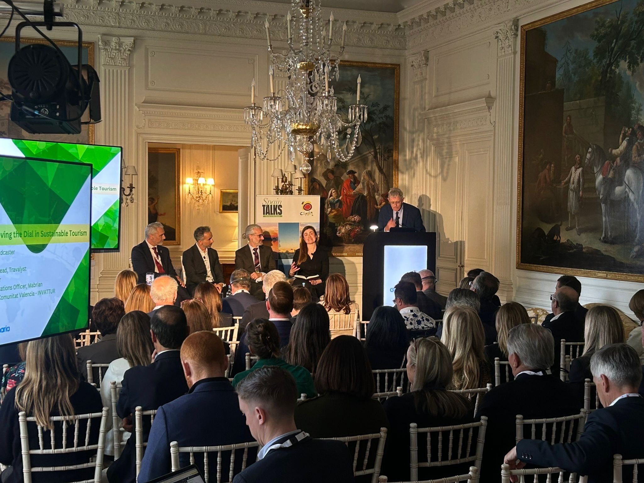 Panelists discuss sustainable tourism at a corporate conference, featuring professional staging, lighting, and sound setup in an ornate room.