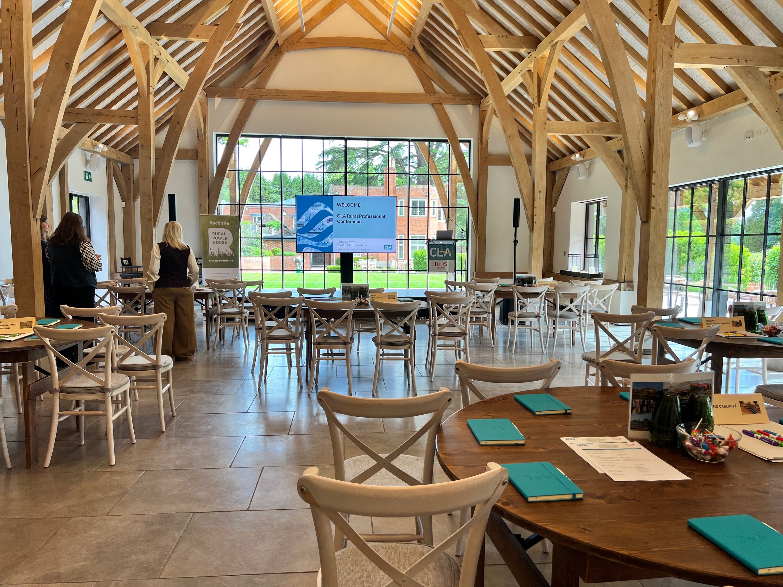Spacious conference hall setup with round tables and chairs, featuring a large presentation screen for a rural professional event.