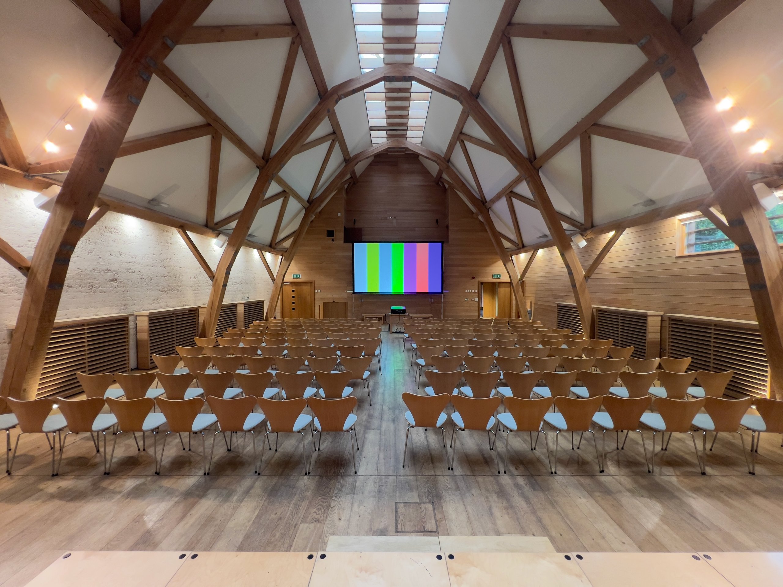 Wooden seminar room setup with rows of chairs facing a large projector screen, ready for a corporate event or conference.