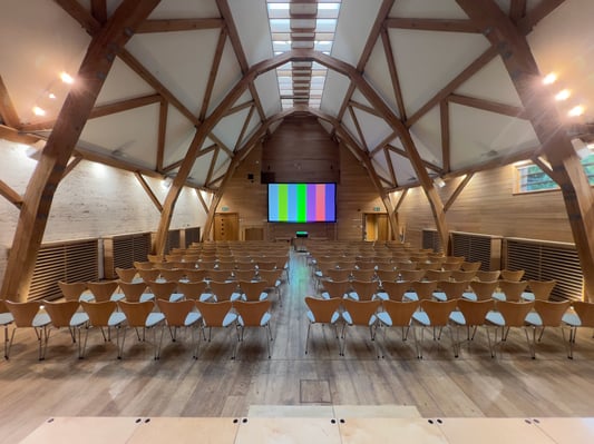Wooden seminar room setup with rows of chairs facing a large projector screen, ready for a corporate event or conference.