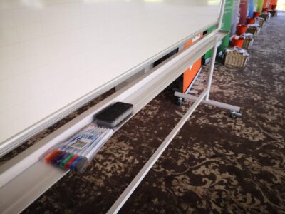 Conference setup with a flipchart, markers, and eraser on a patterned carpet, suggesting a corporate meeting setting.