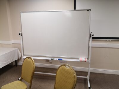 Conference room setup with a large whiteboard, two chairs, and a covered table, suitable for meetings or presentations.