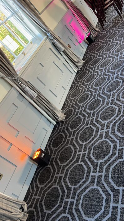 Event space with patterned carpet and colored uplighting against white panel walls, suitable for conferences or receptions.