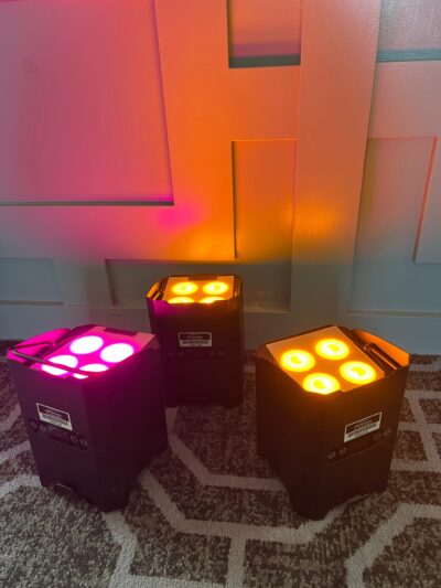 Uplighters projecting colorful beams onto a geometric wall panel, ideal for event atmosphere and dynamic lighting displays.