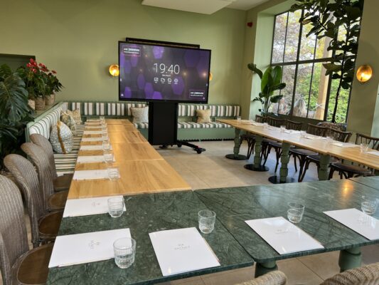 Conference room setup with AV display, polished wood tables, notepads, and glasses, featuring modern decor and large windows.
