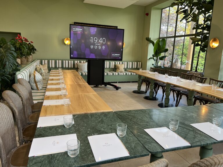 Conference room setup with AV display, polished wood tables, notepads, and glasses, featuring modern decor and large windows.