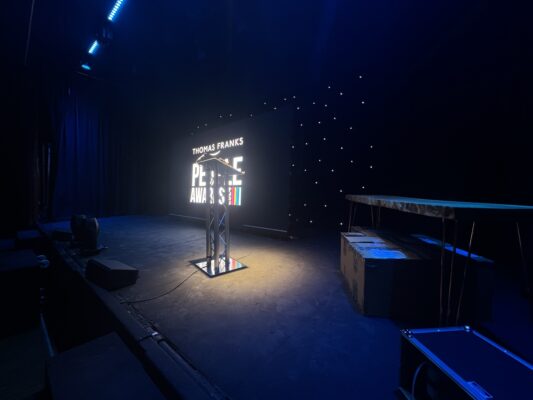 Stage setup for an awards night featuring a lit podium, starry backdrop, and sound equipment, ready for presentations.