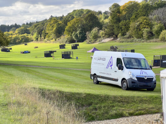 AVE Services van parked on a grassy field with outdoor event structures, ready for event production setup.
