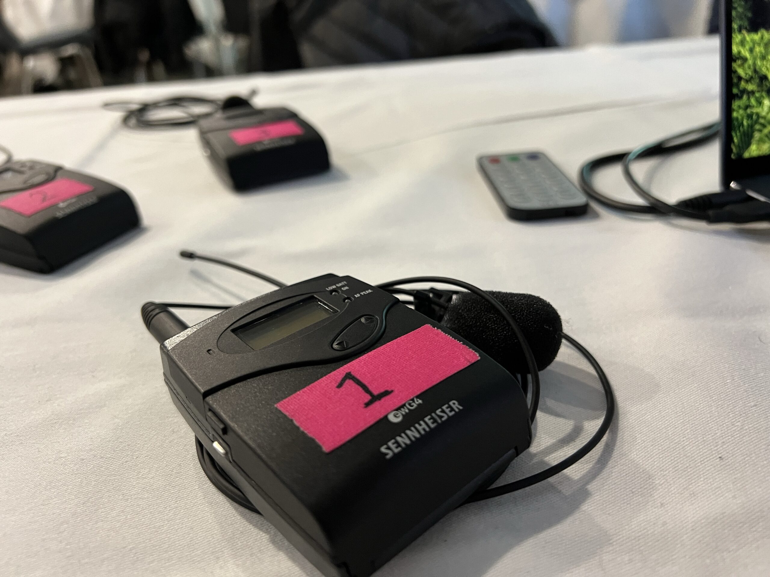 Multiple wireless lapel microphone transmitters labeled with numbers are arranged on a table, ready for event use.