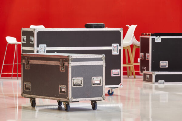 Rolling AV equipment cases on polished floor in a brightly lit event setup area with modern white chairs.