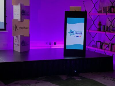 Awards night stage setup with podium and digital display, featuring purple lighting and branded signage.