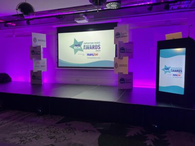 Stage setup for Expedition Cruise Awards 2024 with purple lighting, a large display screen, and podium in an event venue.