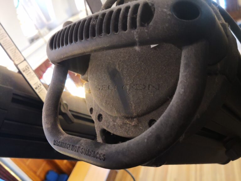 Close-up of stage lighting fixture, highlighting the handle and Warning: Hot Surfaces text, in an event venue.