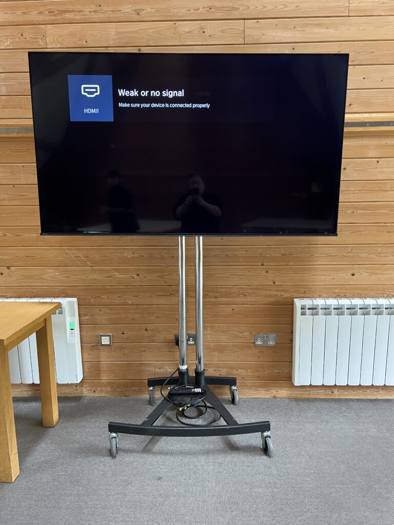 HDMI display screen on stand showing Weak or no signal in a conference setup with wooden panel walls.